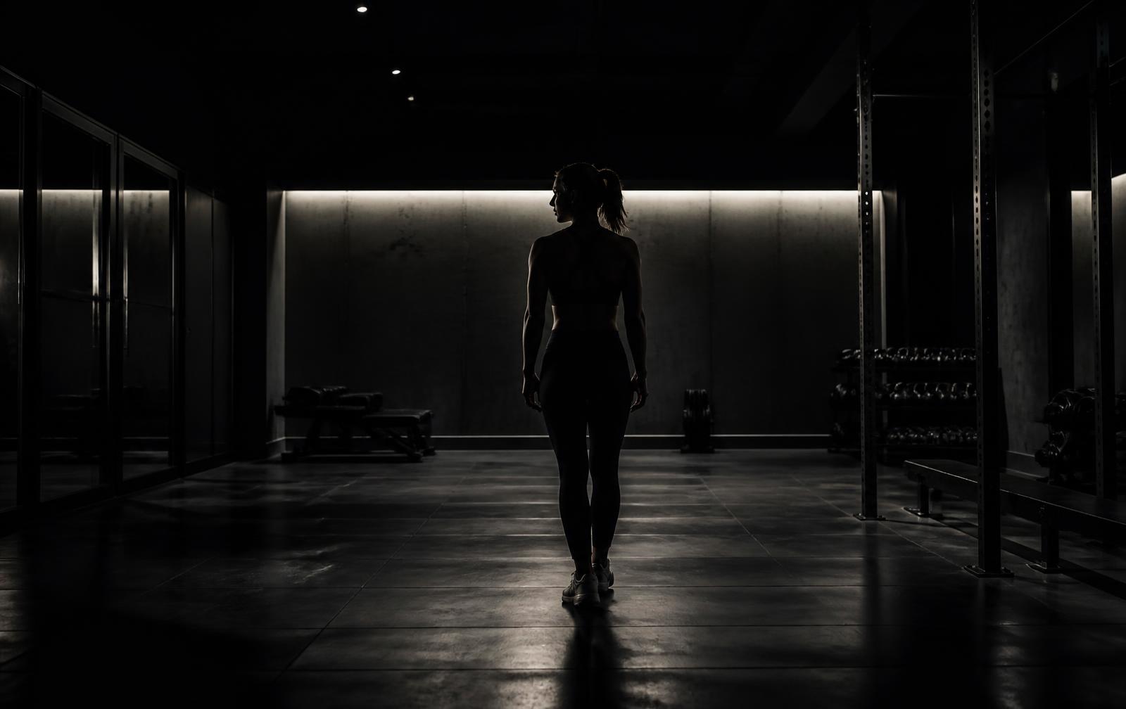 Dimly lit premium fitness studio with a single athlete silhouetted against concrete walls
