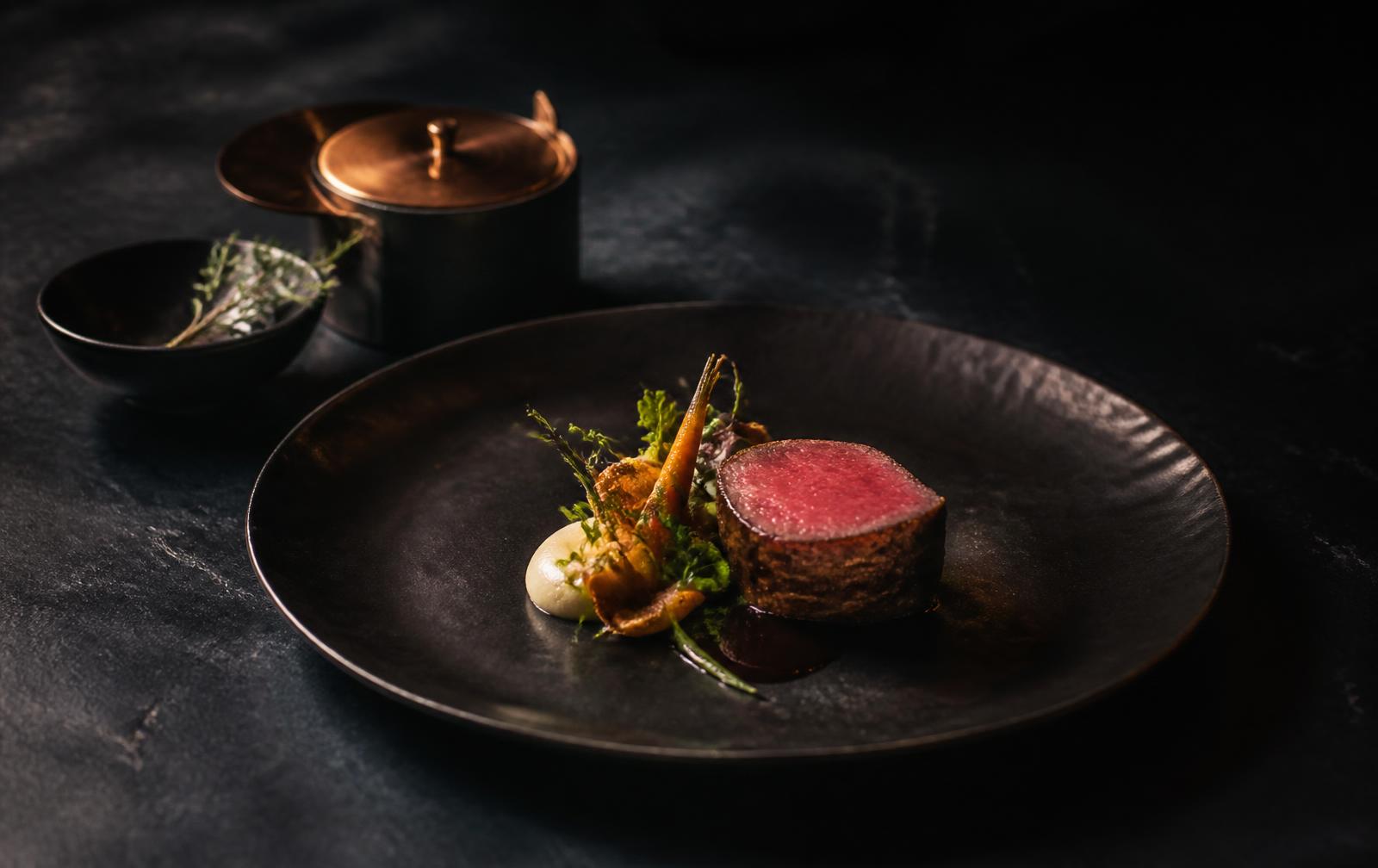 Fine dining plated dish photographed on dark stone with dramatic side lighting